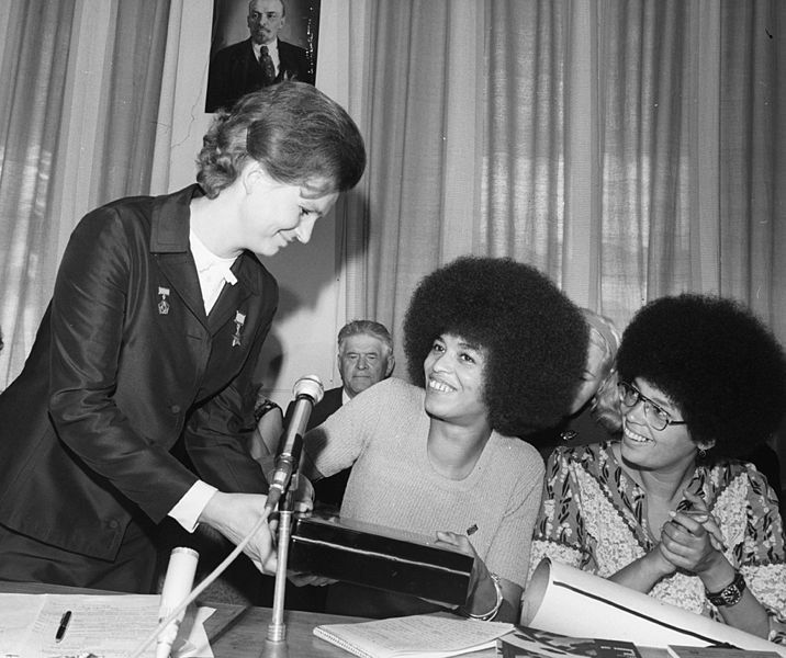 Valentina Tereshkova (standing) presents Angela Davis (seated) with a memento of their meeting.