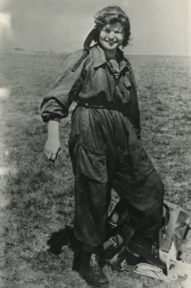 Valentina Tereshkova standing on the ground wearing a jumpsuit and and holding a parachute harness.