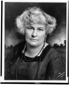 A white woman with grey hair wearing early twentieth century clothing