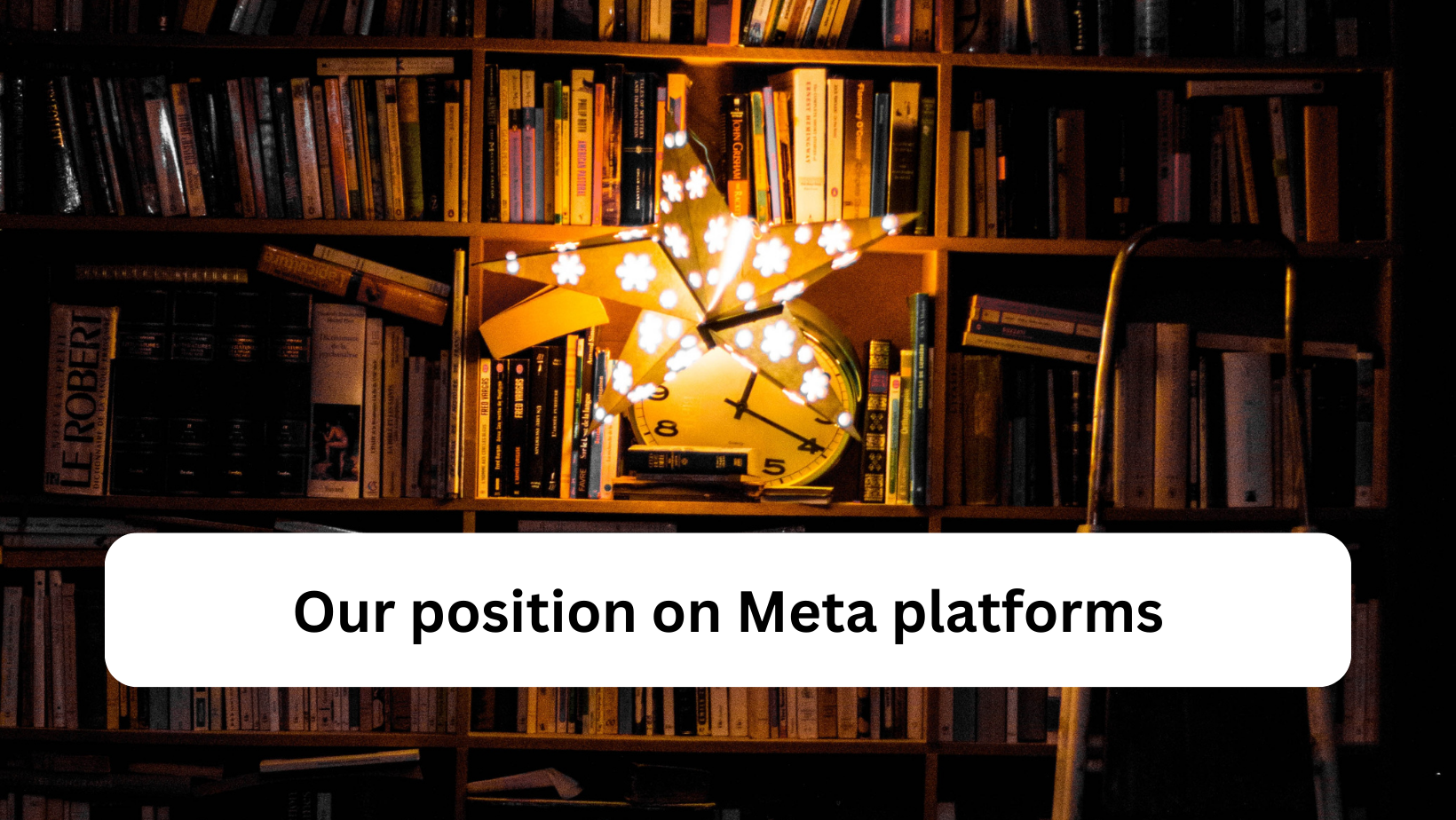 A paper lantern in the shape of a star hangs in front of a dark bookshelf, lighting it. Text on a box reads 'our position on Meta'.